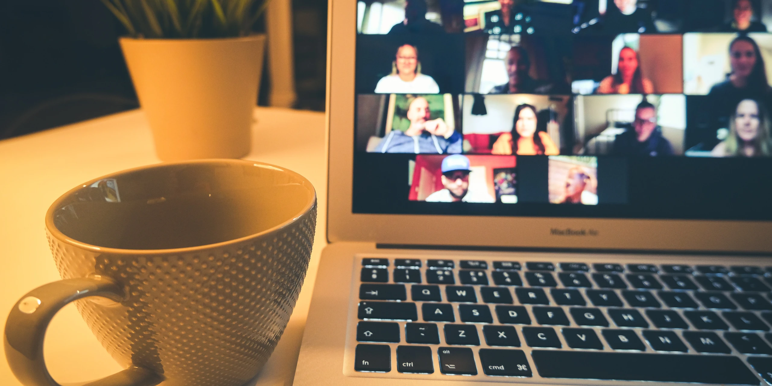 Image of a notebook with online meeting on a screen and coffee mug